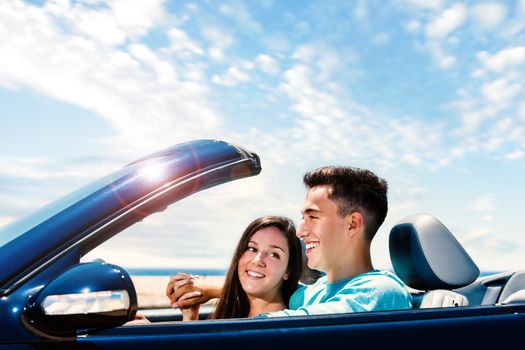 Close up portrait of Happy young couple driving blue convertible along seaside.