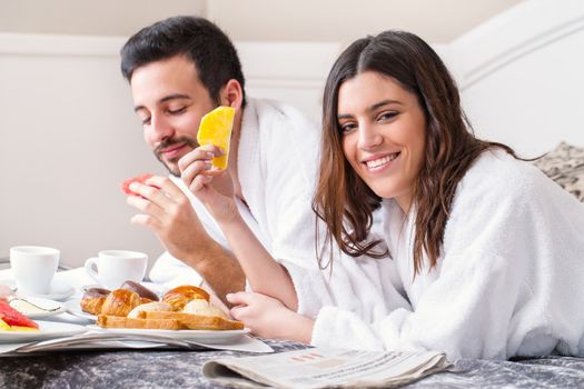 Close up portrait of couple having breakfast together on bed in hotel room.Couple wearing bathrobes.
