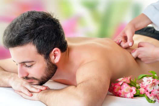 Close up of young man enjoying back massage. Young man laying face down and therapist hands massaging lower back.