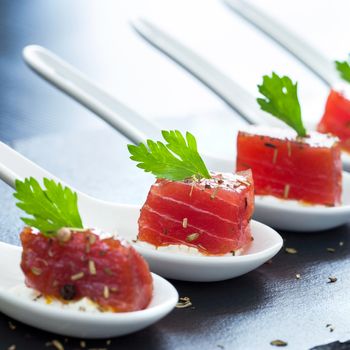 Extreme close up of multiple appetizing tuna dices on white ceramic spoons.