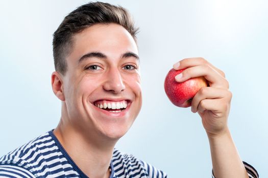 Extreme close up of Handsome young teen holding red apple and  showing healthy teeth.  