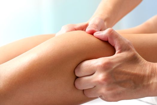 Macro close up of hands doing manipulative healing massage on female calf muscle.