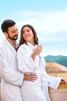 Close up of young couple in bathrobe standing on hotel balcony against rural background.