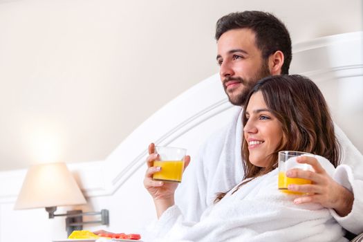 Close up portrait of couple in bathrobe on bed drinking orange juice.
