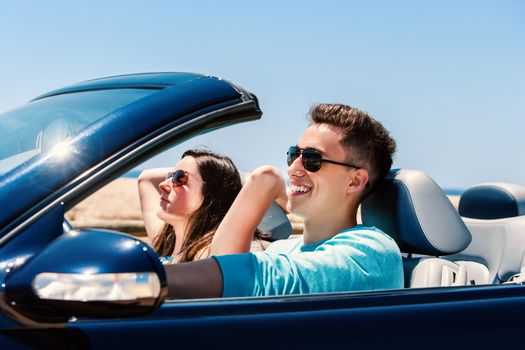 Portrait of attractive young man driving with girlfriend in blue cabriolet.