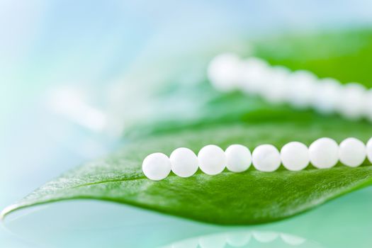 Extreme close up of Multiple homeopathic pills on green leaves against blue background.
