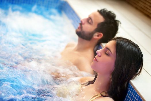 Close up portrait of young couple relaxing in spa jacuzzi. Couple together in bubble water with eyes closed.