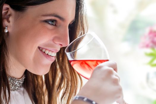 Close up face shot of attractive brunette with charming smile enjoying glass of wine.