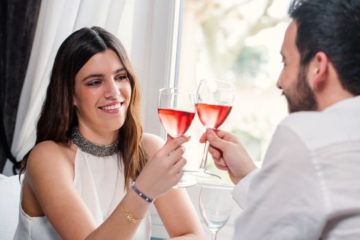 Close up portrait of attractive elegant brunette making a toast with red wine at dinner with boyfriend.