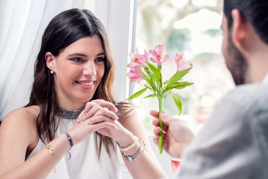 Close up portrait of attractive elegant brunette receiving flower from boyfriend in restaurant.