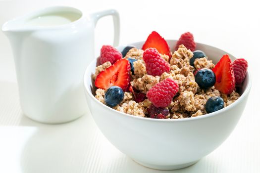 Macro close up of crunchy muesli with red fruit.White bowl with muesli and milk jug in background.