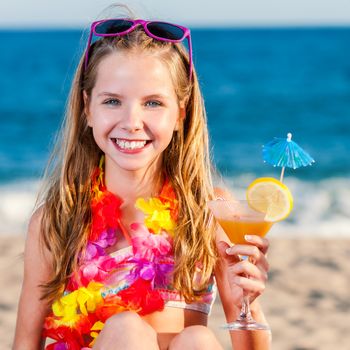 Close up portrait of attractive little preteen girl on beach holding fruit cocktail.