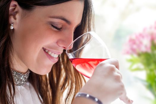 Close up face shot of attractive brunette smelling wine with eyes closed.
