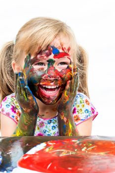 Close up portrait of little girl with painted face. Laughing infant with messed painted hands on cheek. Isolated on white background.