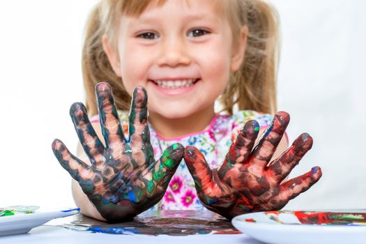 Close up portrait of little girl showing hands messed with color paint at table.Isolated on white background.