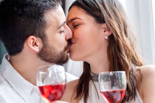 Close up face shot of couple kissing at romantic dinner. Out of focus wine glasses in foreground.