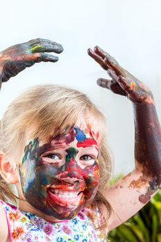 Close up portrait of little girl covered with color paint raising hands above head.