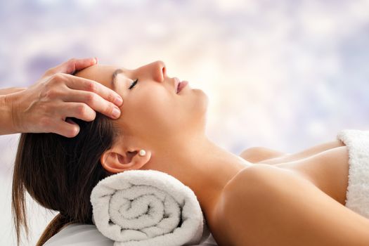 Close up portrait of attractive young woman having relaxing facial massage. Therapist massaging woman’s head against bright colorful background.