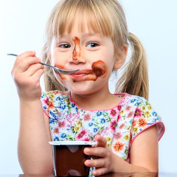 Close up portrait of Cute little girl eating chocolate yogurt at breakfast. Face messy with chocolate and naughty facial expression.
