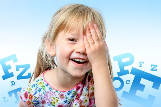 Close up fun portrait of little girl closing on eye with hand.Big block letter conceptual eye chart in background.