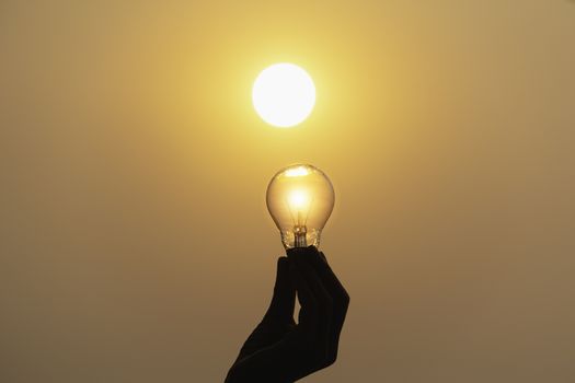 Hand hold a light bulb on sunset background for saving energy and creative concept.