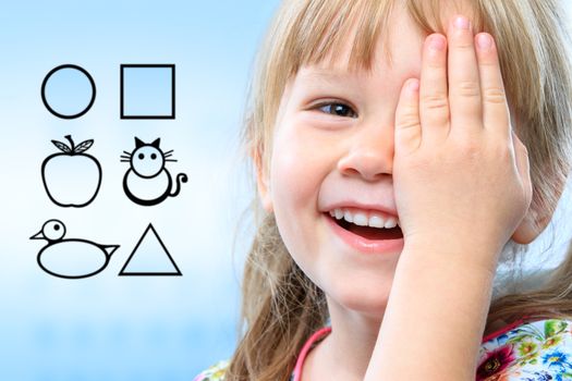 Close up face shot of little girl closing one eye with hand. Childish symbols in background as vision test chart.