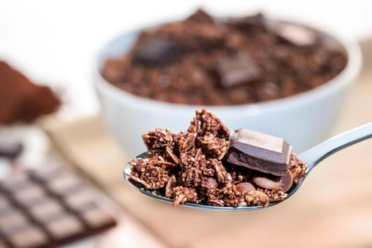 Extreme close up of Spoon with crunchy chocolate muesli and bowl in background.