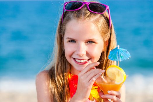 Close up head portrait of attractive little girl drinking fruit cocktail on beach.