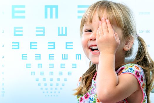 Close up fun portrait of little girl testing eye sight.Vision test chart in background.
