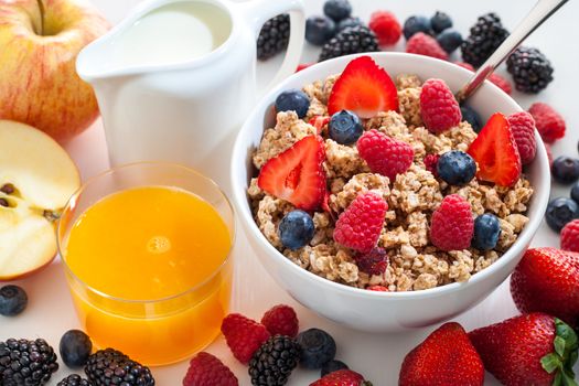 Macro close up of appetizing crunchy muesli bowl with red fruit. Fruits and fresh orange juice next to bowl.
