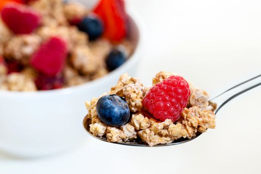 Extreme close up of spoon with crunchy red fruit muesli and bowl in background.