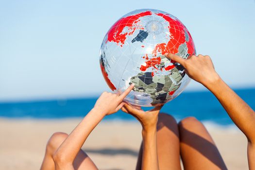 Close up of female hands holding and pointing at inflatable earth ball on beach.
