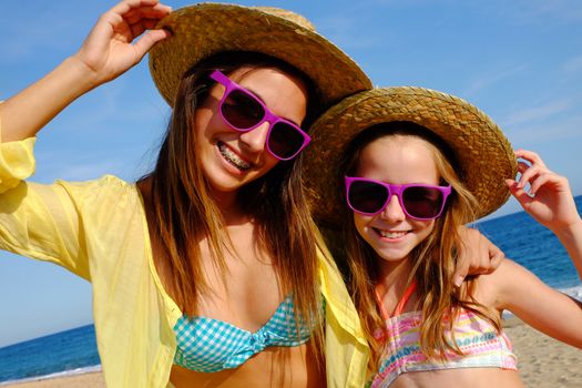 Close up outdoor portrait of attractive young mother and daughter on beach wearing straw hats and fun purple sunglasses.