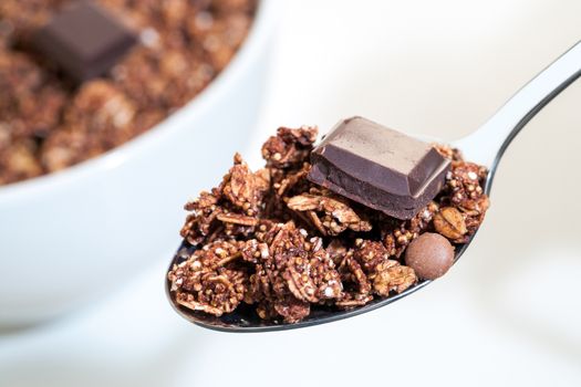  Macro close up of spoon with crunchy chocolate muesli and out of focus bowl in background.