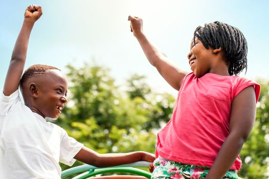 Close up portrait of two happy African kids looking at each other raising hands outdoors.
