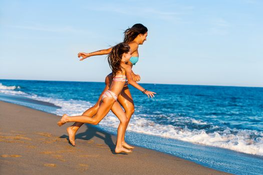 Action portrait of Young girls on holiday. Two women running towards blue sea.