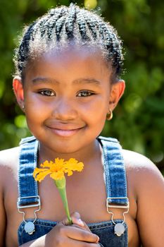 Close up portrait of cute little african girl with braided hairstyle holding orange flower outdoors.