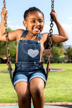 Close up portrait of little smiling African girl swinging in park.
