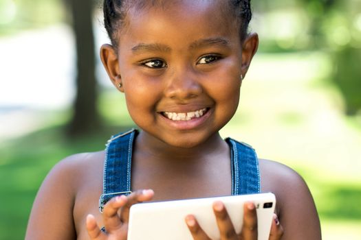 Close up outdoor portrait of cute little african girl playing on digital tablet.