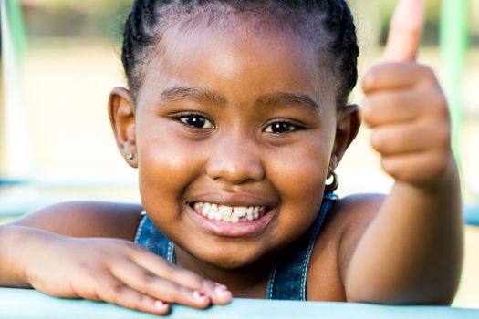 Close up face shot of little african girl doing thumbs up outdoors.
