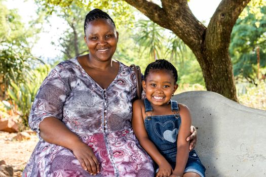 Close up portrait of african mother and child sitting on bench in park.