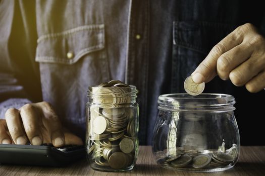 Hand putting money coin in the glass jar. Saving money, financial and accounting concept.