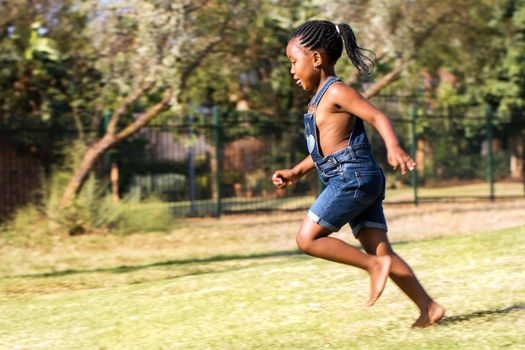 Close up action portrait of african kid running in park. Side view of little ponytailed girl in motion.