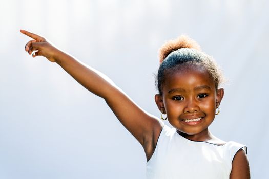 Portrait of little African girl pointing at corner with finger.Isolated against light background.