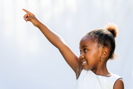 Portrait of little African girl pointing with finger and looking at corner.Isolated against light background.