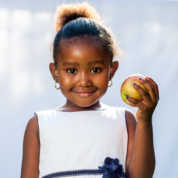 Close up portrait of cute African girl holding apple in hand.Isolated against light background.