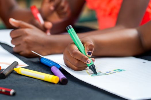 Macro close up of African kids hands drawing with wax crayons at desk.