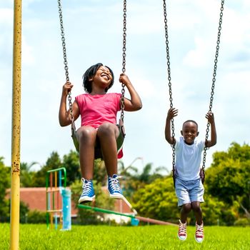 Action portrait of African kids having fun swinging in park.Out of focus houses in background.