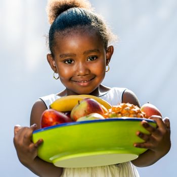 Portrait of sweet Afro American girl with fruit bowl.Isolated against light background