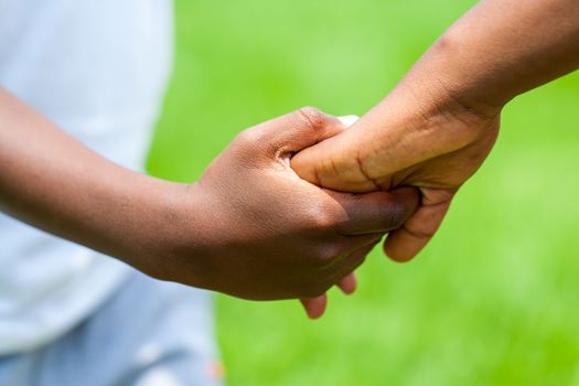 Macro close up Detail of African boy holding girls hand against green outdoor background.